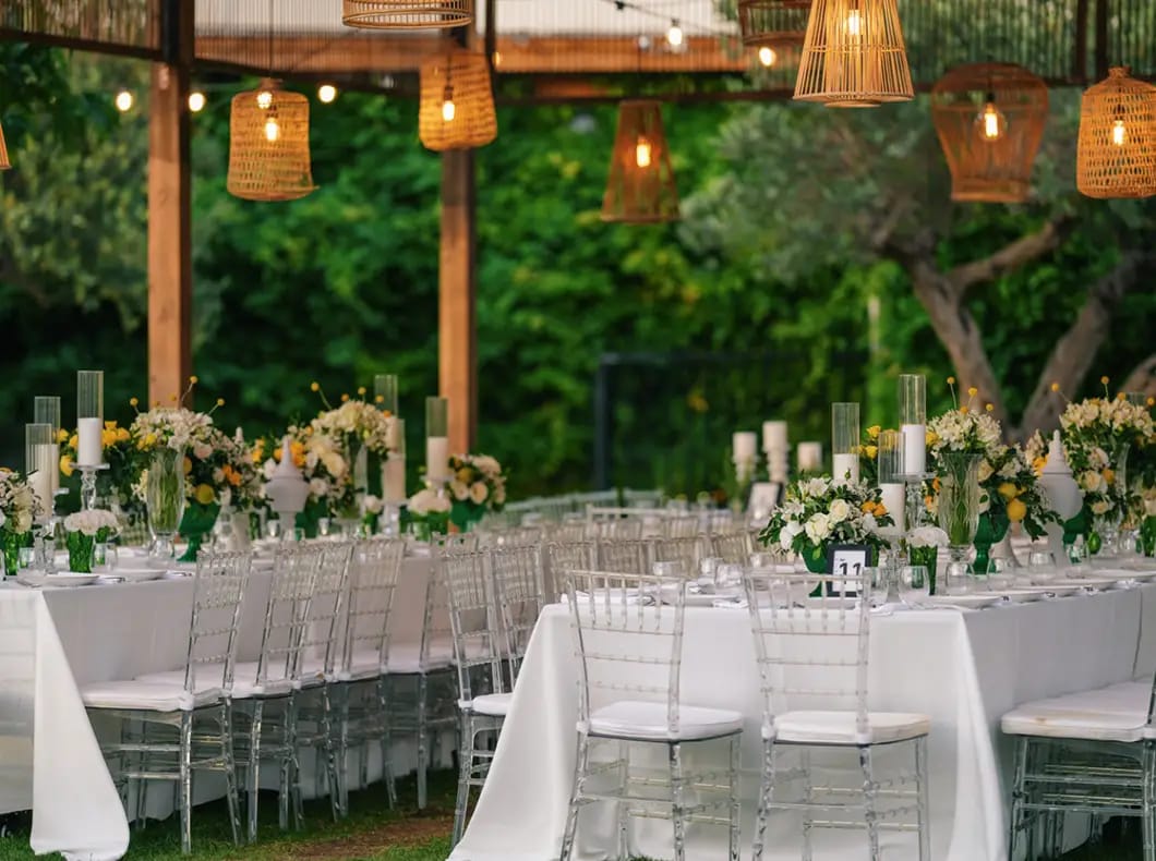 Longues tables en lin blanc et chaises transparentes sous une pergola en bois ornée de lanternes tressées au Bustan