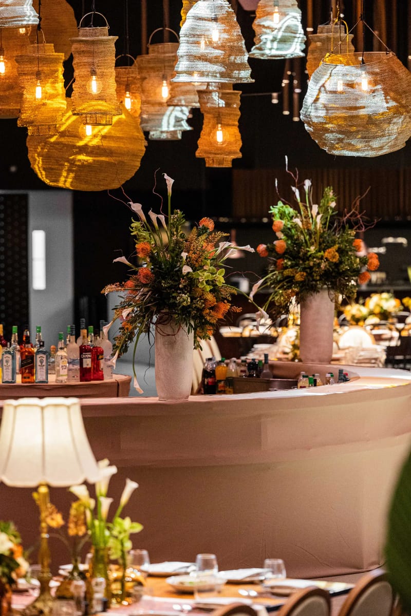 Lanternes ambrées et en verre suspendues au-dessus d'un bar rond à jupe rose, lampes et fleurs orange