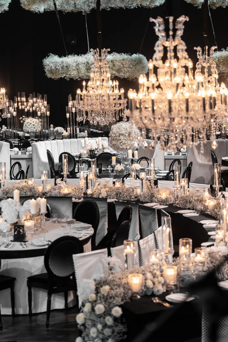 Grands lustres en cristal et anneaux floraux suspendus au-dessus d'une table de banquet courbe, chemin de fleurs blanches et bougies