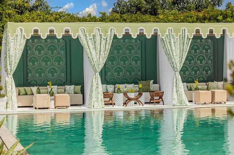 Cabane à auvent festonné vert et blanc, rideaux à motif feuillagé et canapés au bord du bassin