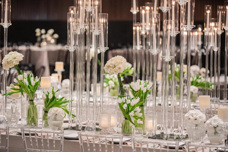 Tall clear glass candle holders and white tulips on a long banquet table in the Ivory Luxe design