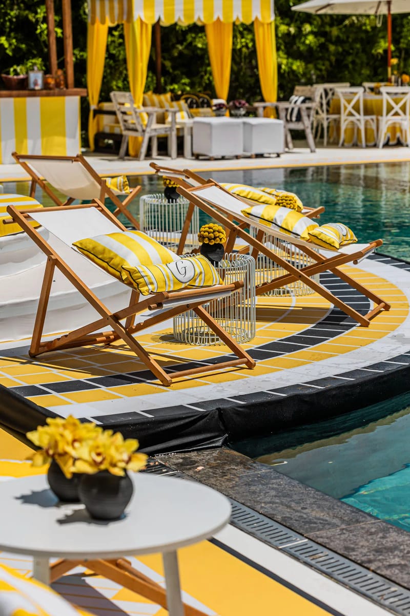 Deck chairs with yellow striped cushions on a round platform by the pool, and a small table with yellow flowers
