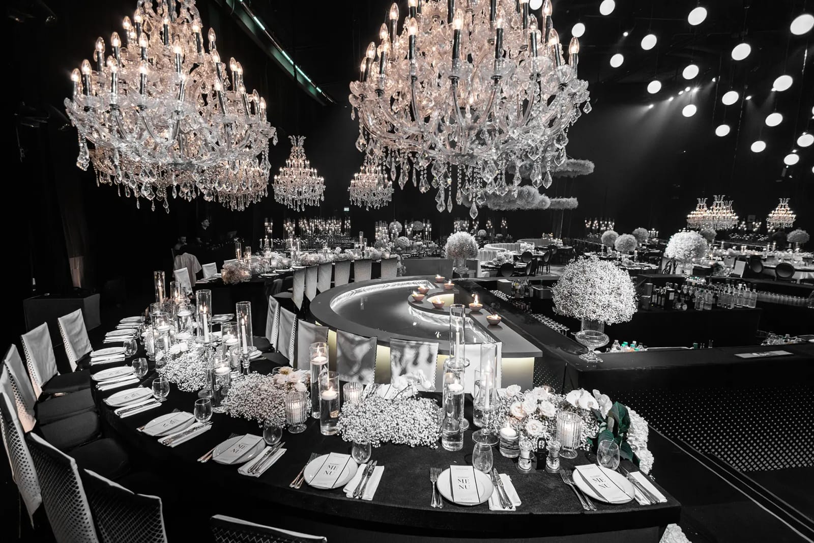Deux grands lustres en cristal au-dessus d'une longue table noire courbe avec compositions de gypsophile blanche et bougies