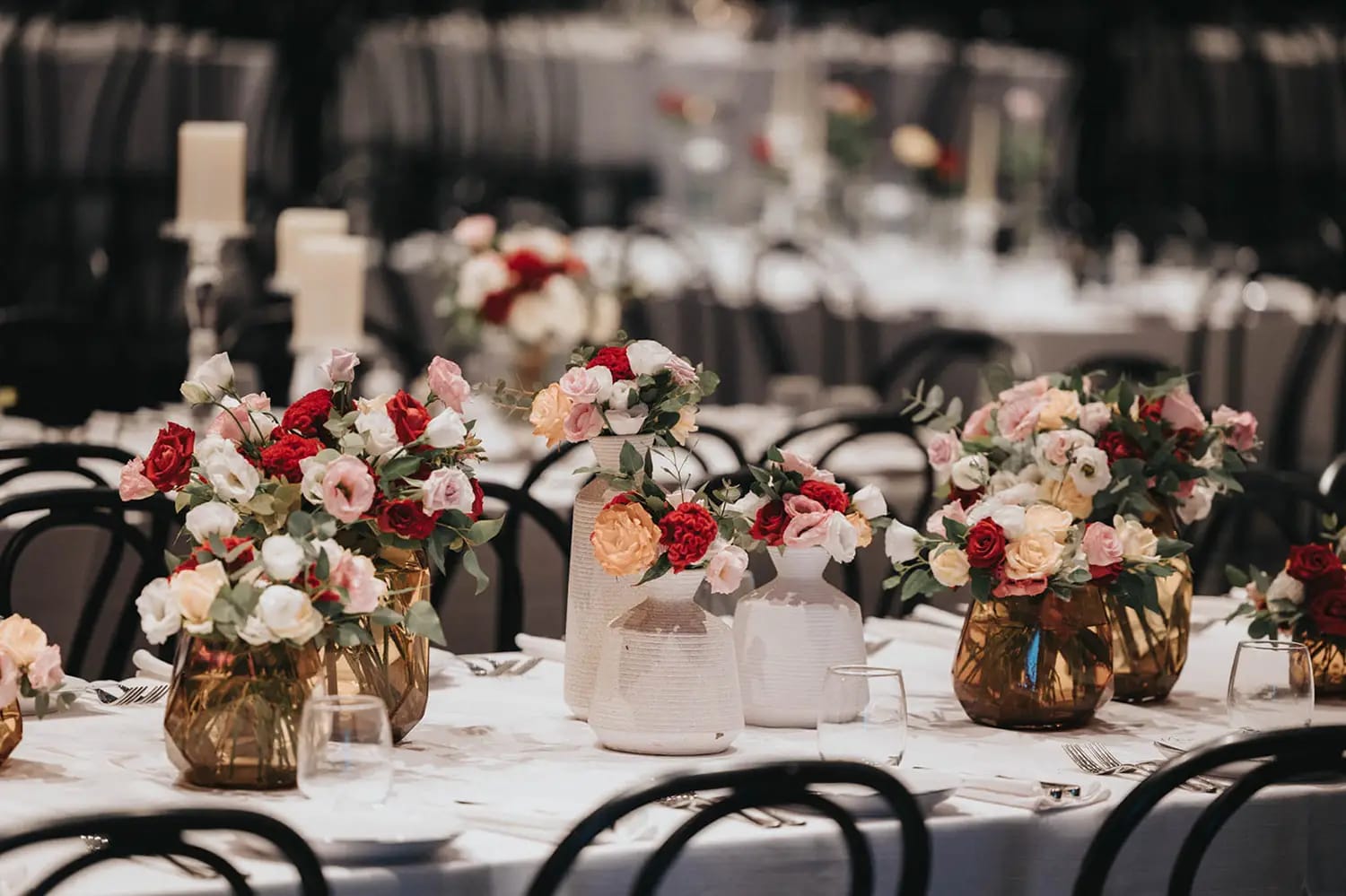 Gros plan sur des roses rouges, roses et pêche dans des vases dorés et blancs avec bougies pilier sur une table blanche