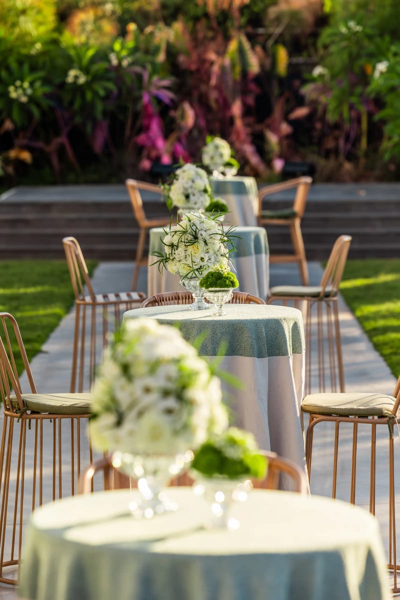 Cocktail tables with pale-blue cloths and white-and-green floral arrangements on the lawn, with bar stools