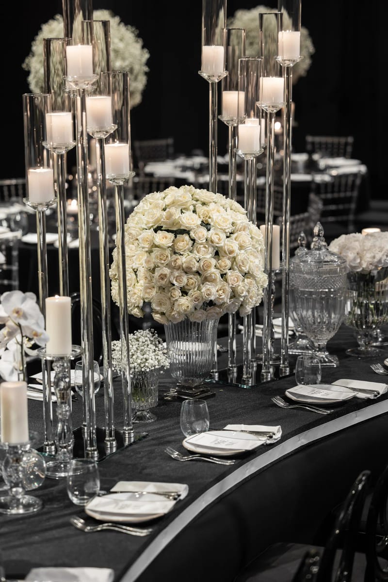 Hauts photophores transparents et grand bouquet de roses blanches sur une table courbe à nappe noire