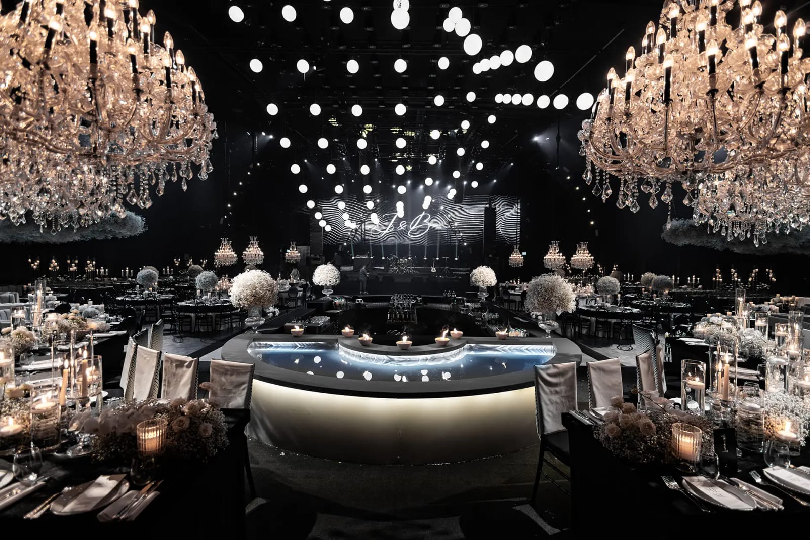 Salle sombre avec lustres en cristal de chaque côté, plafond de lumières globes et comptoir courbe lumineux entre les tables