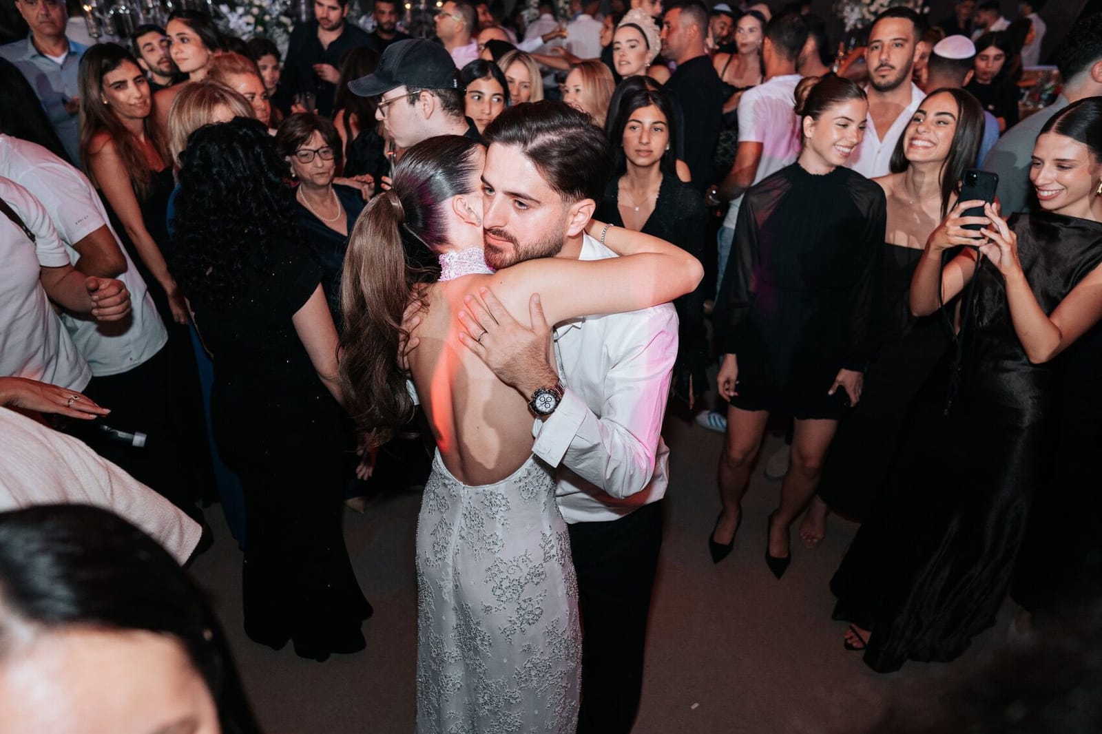 Un couple enlacé sur la piste de danse, entouré d'invités qui l'acclament et filment