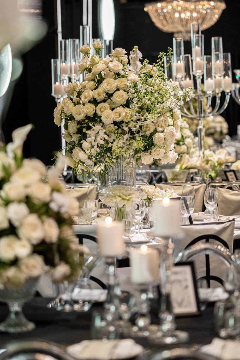 Roses blanches et chandelier en verre sur une table dressée sous un lustre en cristal, avec des chaises noires