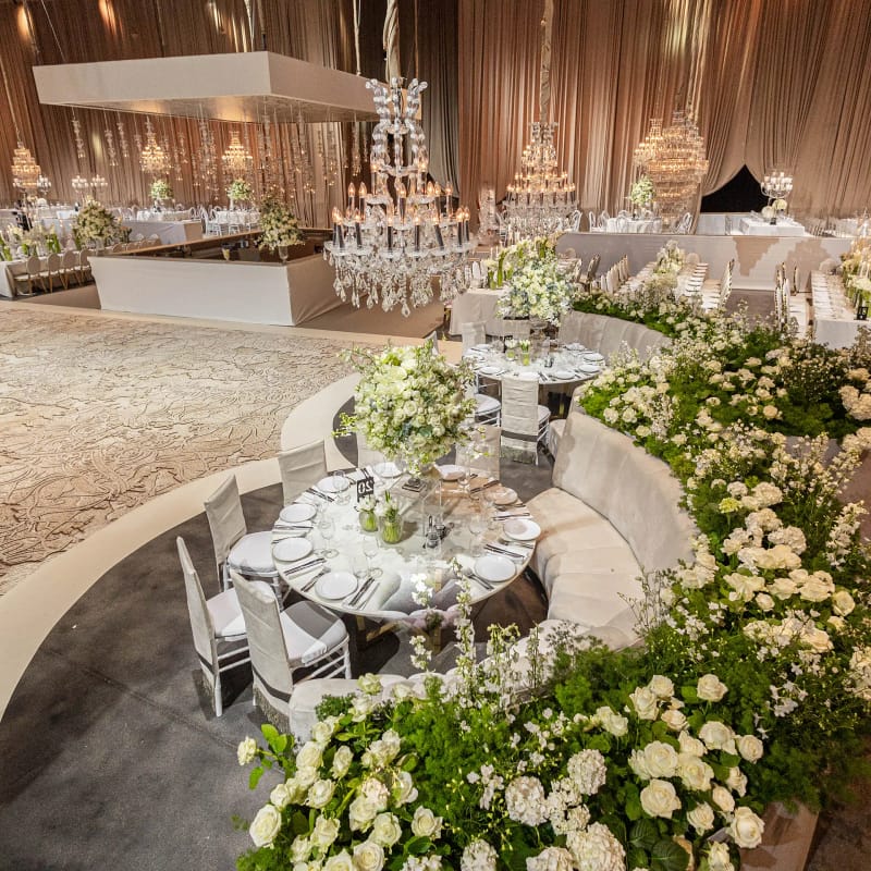 Banquette courbe garnie de fleurs blanches, table ronde aux chaises argentées et lustre en cristal au-dessus de la piste