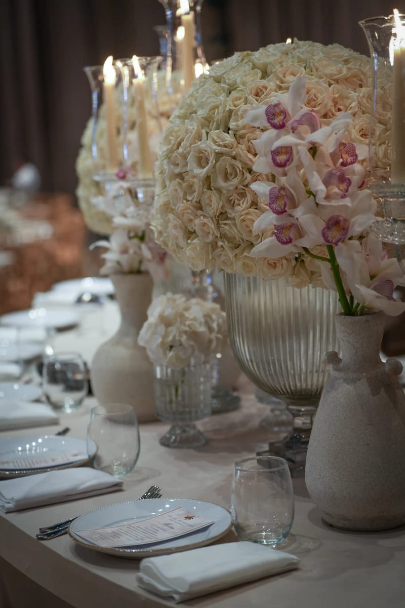 Roses claires et orchidées roses dans une urne en verre sur une table dressée, près de vases en céramique et d'une assiette