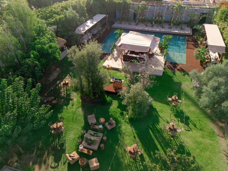 Aerial view of a garden with a pool, a fabric pavilion, lawn seating groups and trees