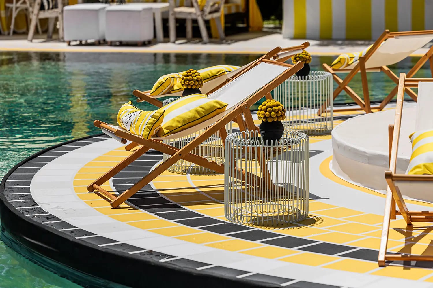 Deck chairs with yellow cushions on a curved yellow-tiled platform in the pool, with a striped cabana behind
