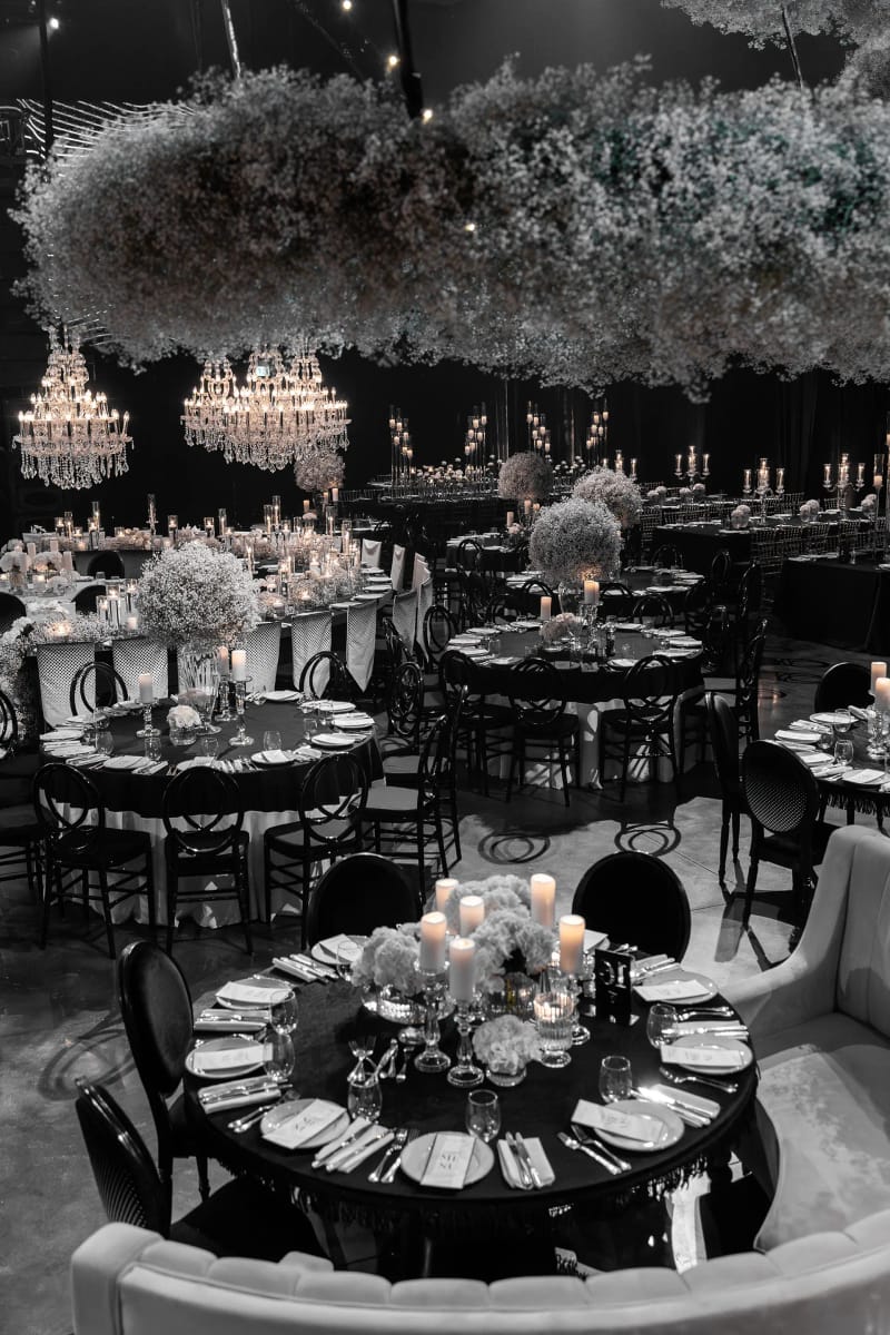 Nuage de gypsophile suspendu au-dessus de tables rondes, chaises noires et banquette courbe, en tons presque monochromes