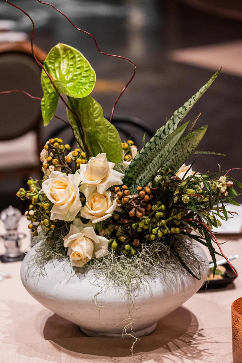 Gros plan sur des roses crème, des feuilles vertes et des baies dans une coupe blanche sur une nappe claire