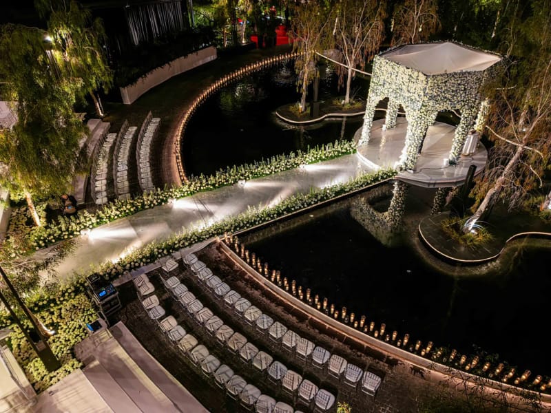 Vue aérienne de nuit d'un pavillon de fleurs blanches au bout d'une allée éclairée, avec des chaises en arc autour du bassin