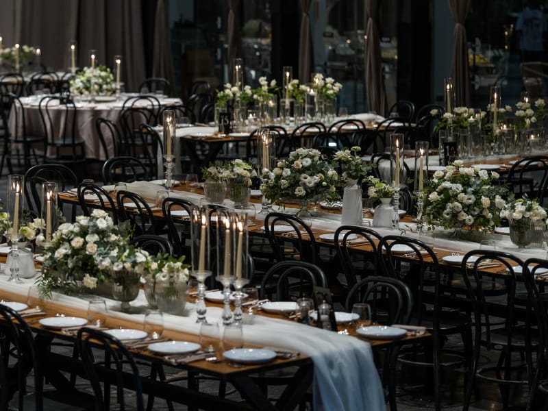 Shulhan hall with long wooden tables, white runners, black chairs, candles and floral arrangements