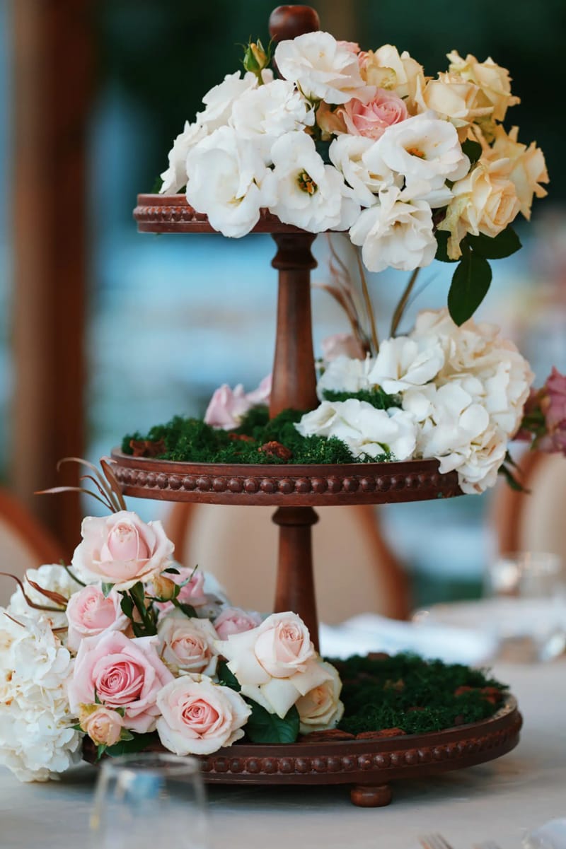 Two-tier wooden stand holding white and pink roses and moss, against a softly blurred background