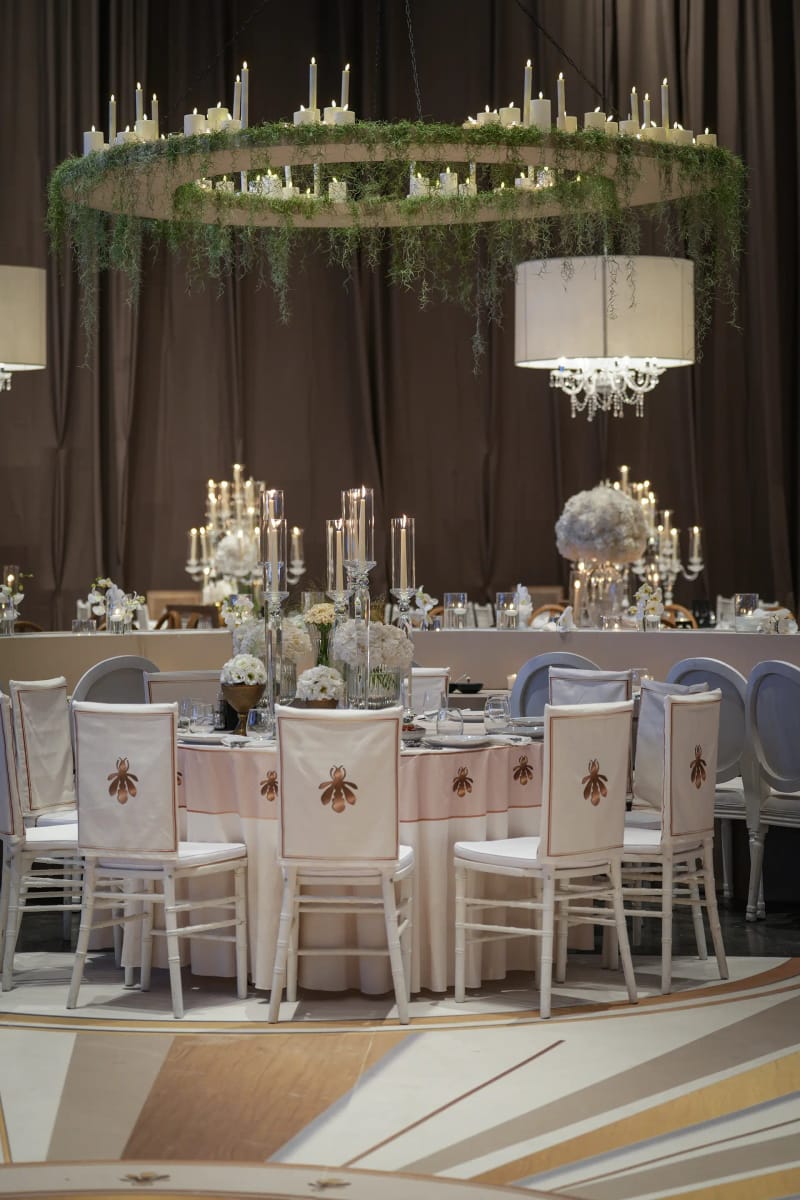 Couronne de verdure avec bougies suspendue au-dessus d'une table ronde et de chaises blanches, sur un sol à motif de rayons