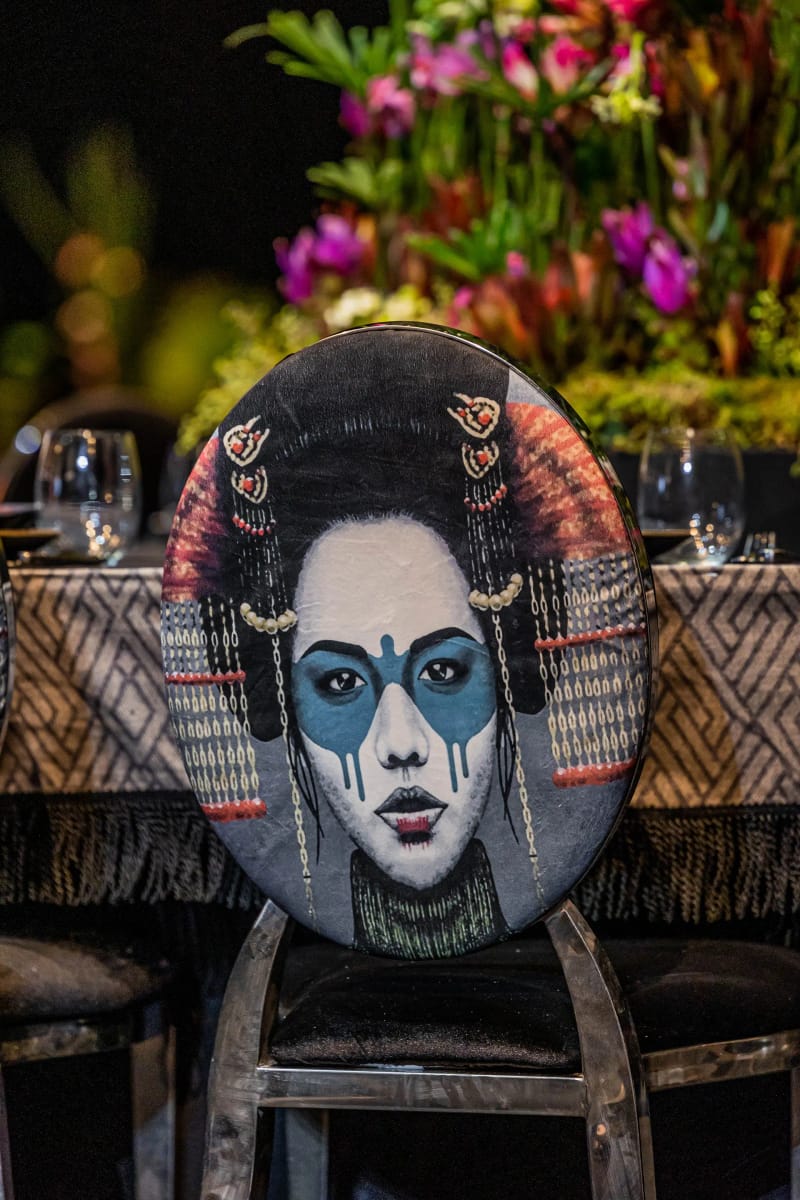 Chair back decorated with a painted portrait with a blue mask and ornate headdress, pink flowers above
