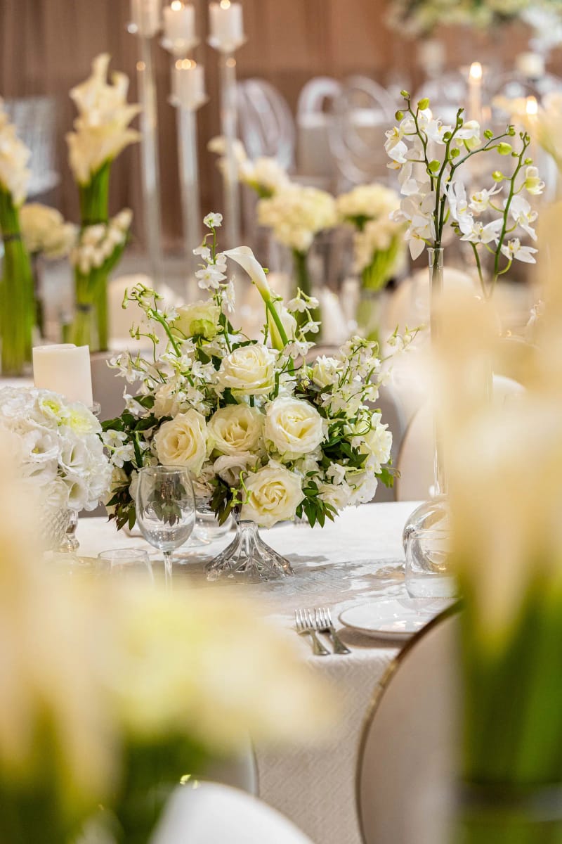 Centre de table de roses blanches et de callas, avec des bougies floues à l’arrière-plan